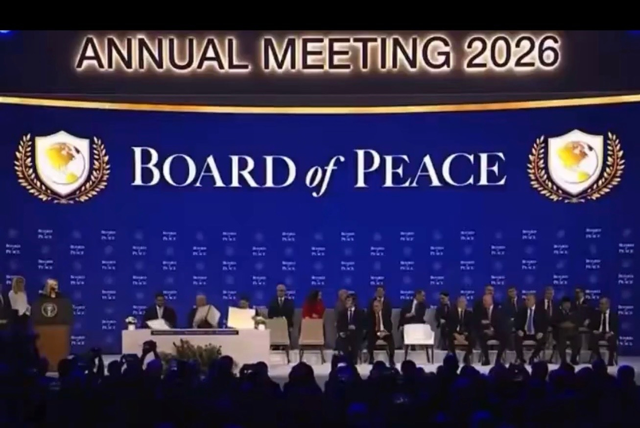 A group of people is seated onstage under a large sign that reads Annual Meeting 2026 Board of Peace with official insignia.